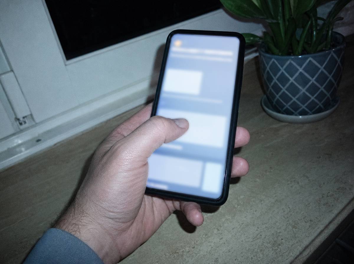 Kciuk przesuwający po ekranie telefonu z nieczytelną treścią, kuchnia w tle