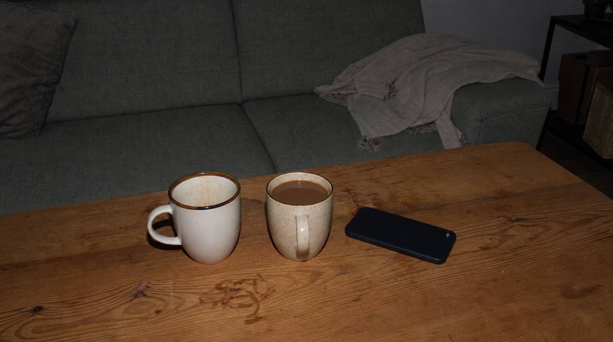 Dwa kubki na stole, jeden nietknięty, i telefon ekranem do blatu po rozmowie w związku
