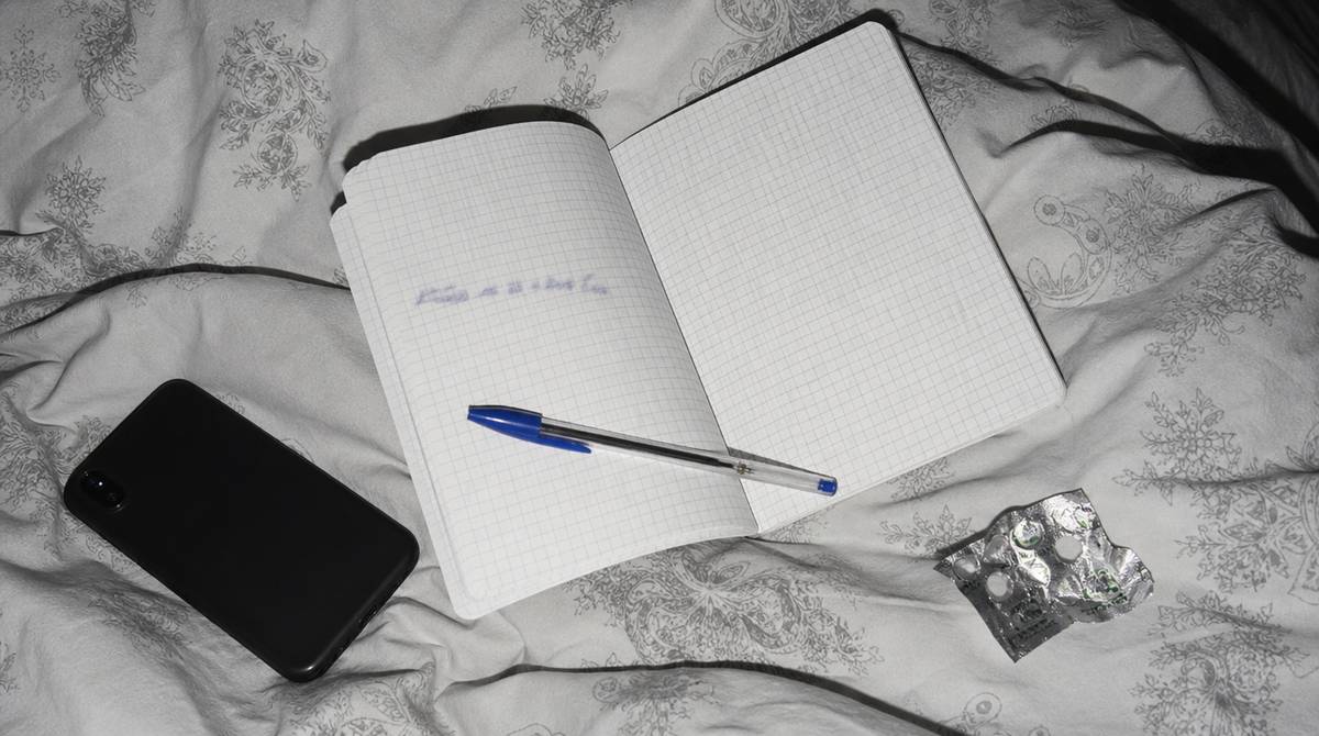 Notes z zapisanym zdaniem intencji, długopis i telefon ekranem do dołu na kołdrze nocą