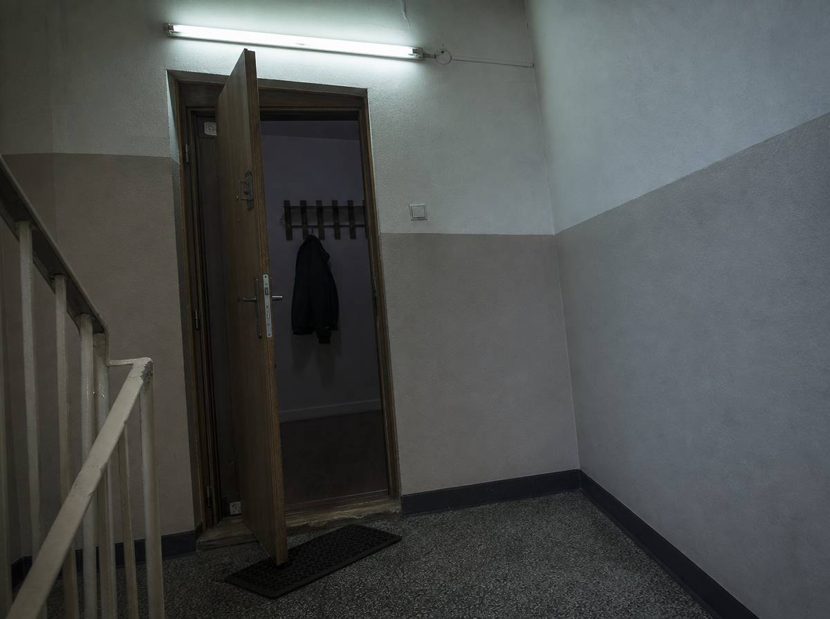 Drewniany próg uchylonych drzwi mieszkania widziany z klatki schodowej, przekrzywiona wycieraczka