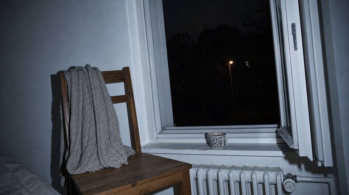 Puste krzesło przy uchylonym oknie sypialni nocą, koc na oparciu i stygnący kubek na parapecie